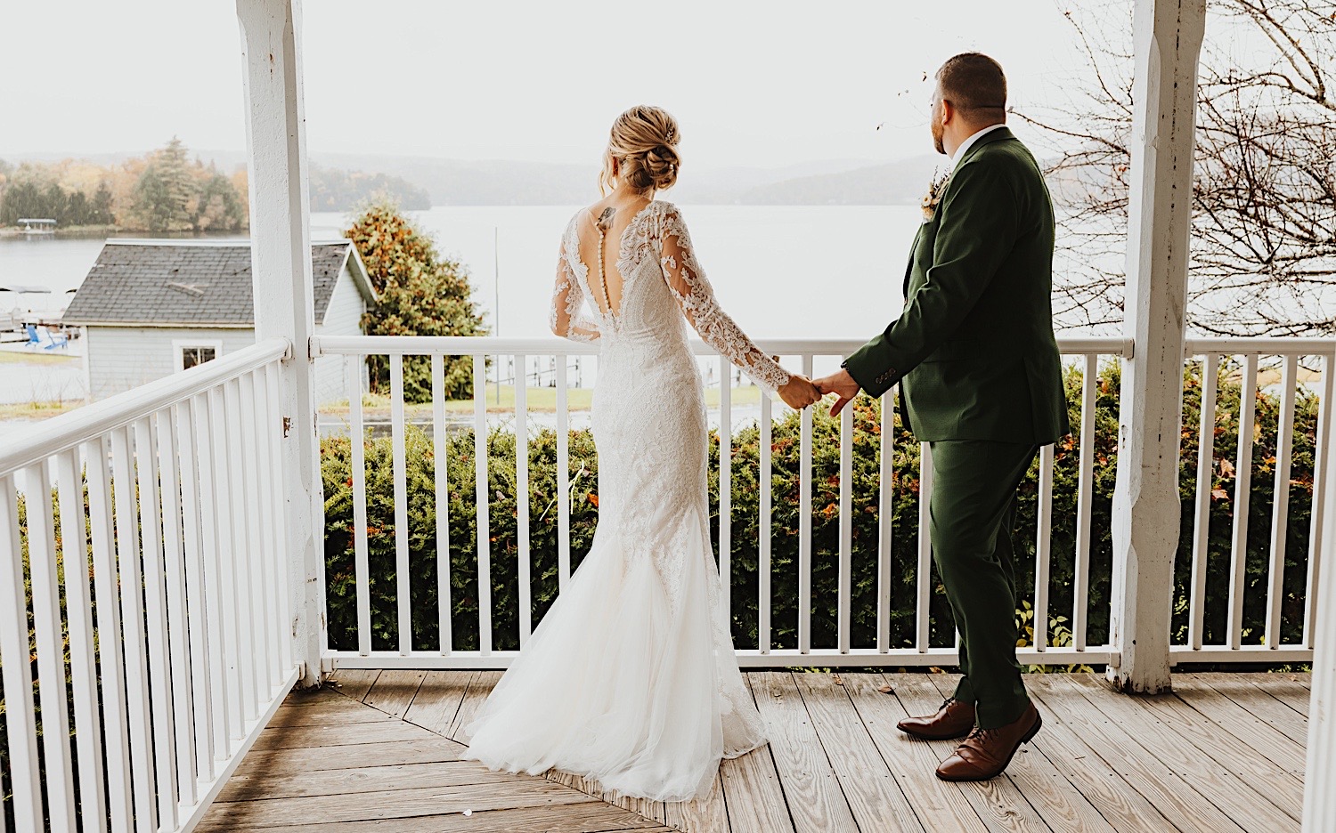 A bride and groom hold hands while looking out at Lake Bomoseen from the front porch of a house