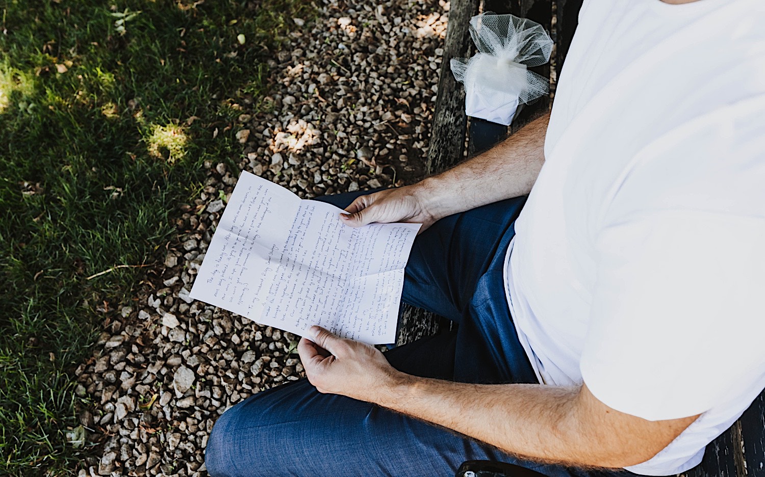 A man holds a letter and reads it while sitting on a bench outdoors