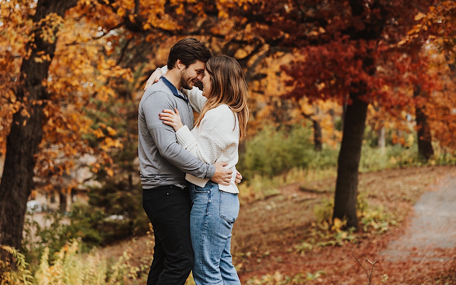 A couple embrace and smile at one another during their engagement session at Theodore Wirth Park in Minneapolis