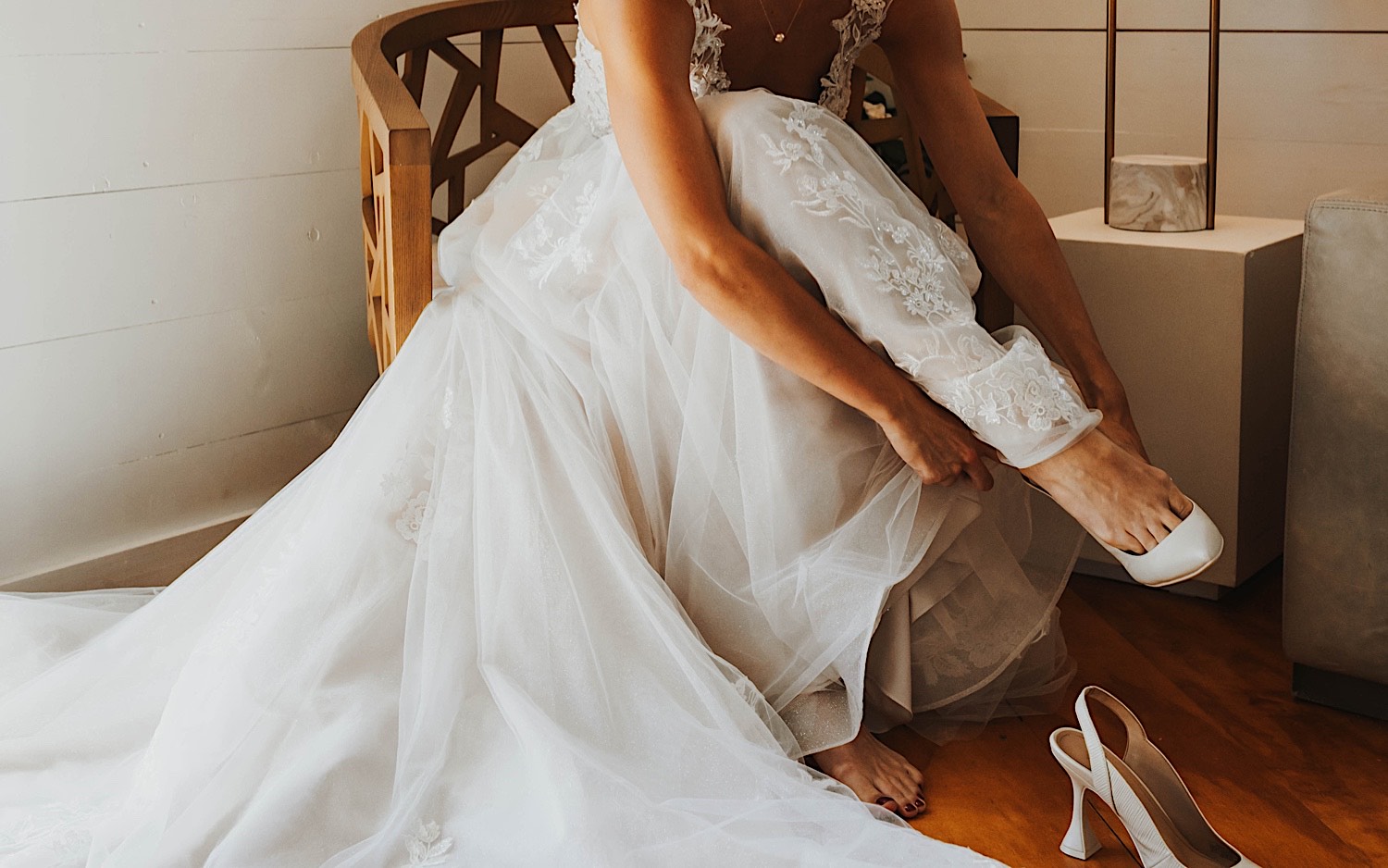 A bride sits in a chair in her wedding dress and puts on her shoes while in the getting ready space at Legacy Hill Farm A bride sits in a chair in her wedding dress and puts on her shoes while in the getting ready space at Legacy Hill Farm