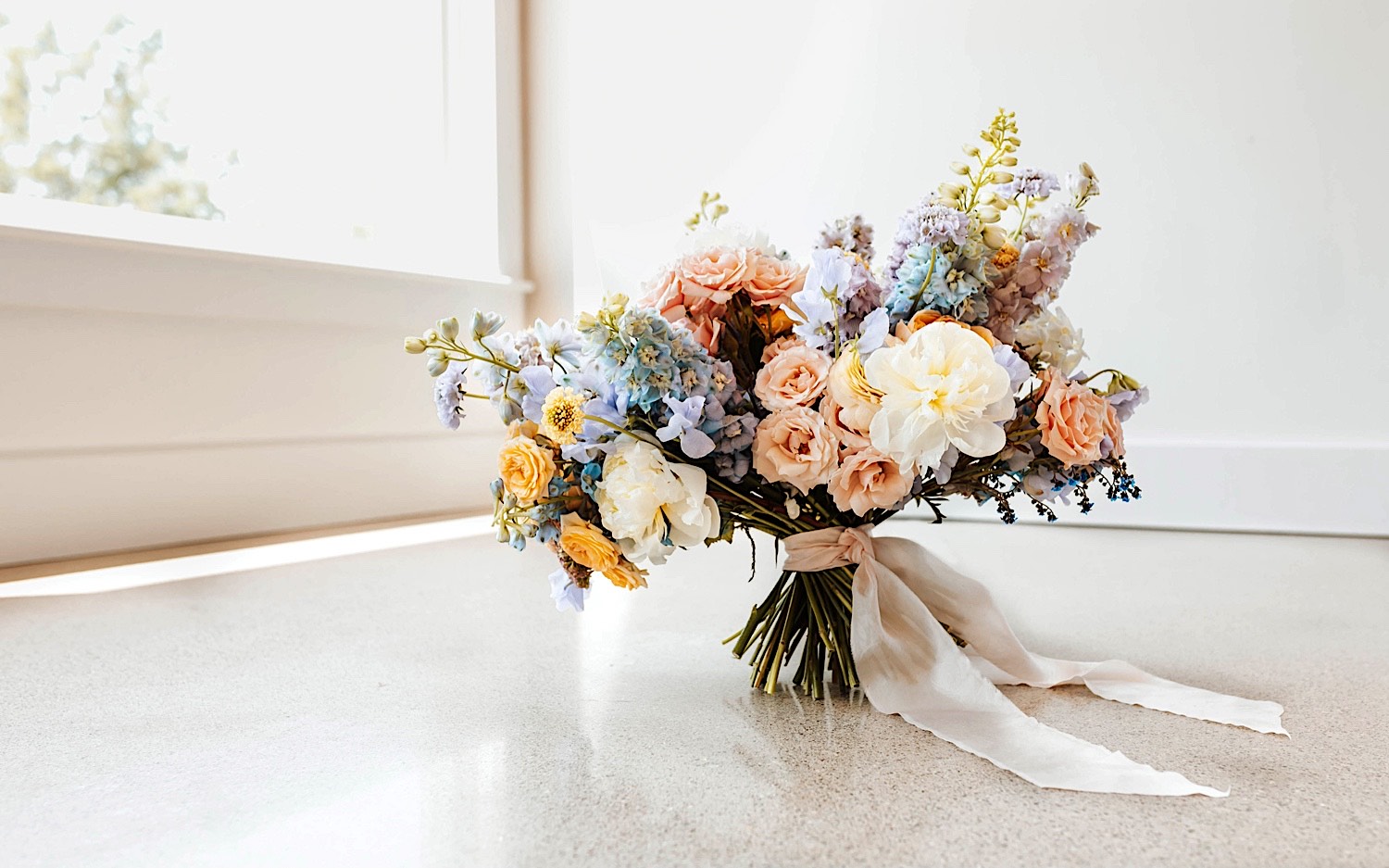 A bouquet of flowers sits on the floor in front of a window