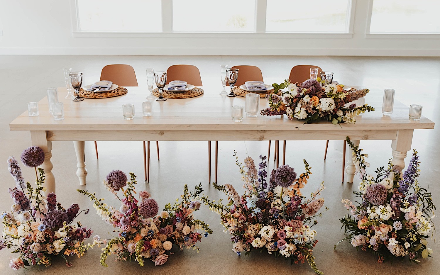 A table set up for a wedding with glassware, floral decorations line the floor in front of the table