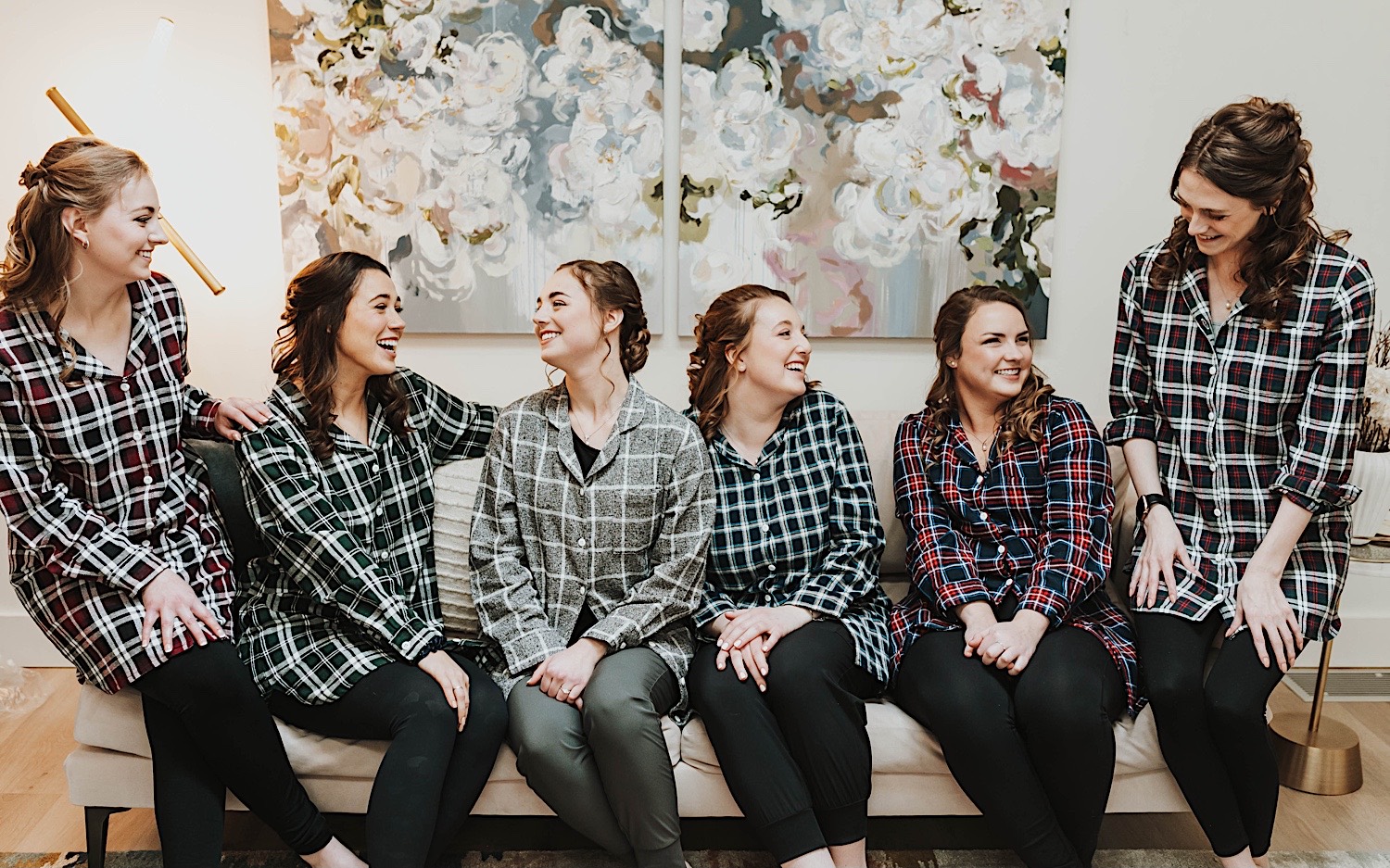 A bride sits on a couch in the getting ready space of Woodhaven Weddings + Events alongside her bridesmaids as they all laugh together