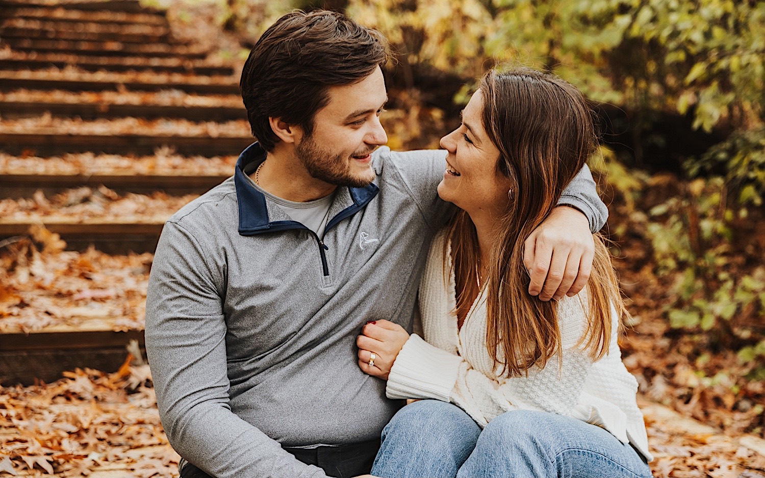 A couple sit together on a wooden staircase inside of Theodore Wirth Park of Minneapolis during their engagement session