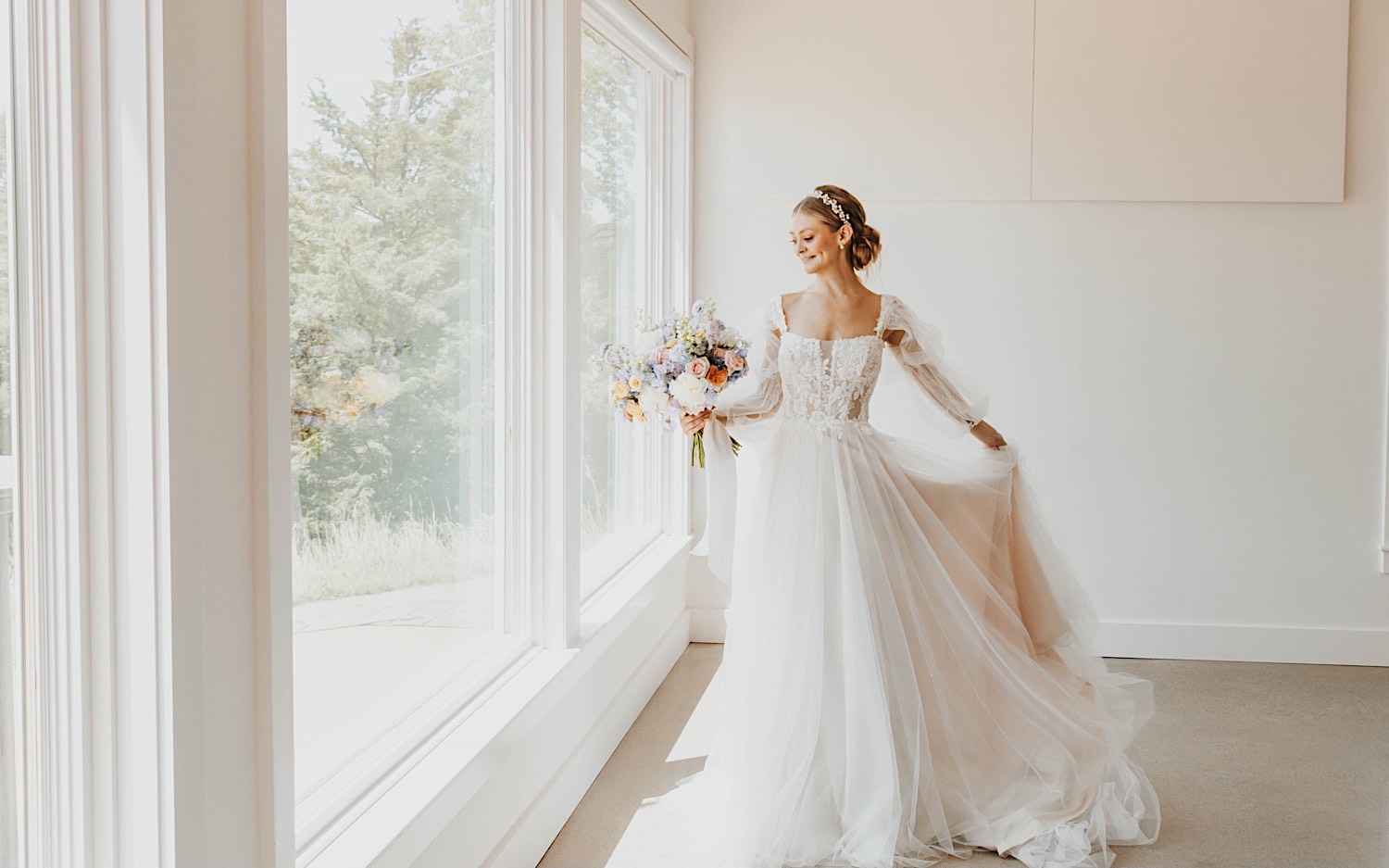 A bride stands in front of a window holding her bouquet and playing with her wedding dress during her wedding day at The Aisling A bride stands in front of a window holding her bouquet and playing with her wedding dress during her wedding day at The Aisling