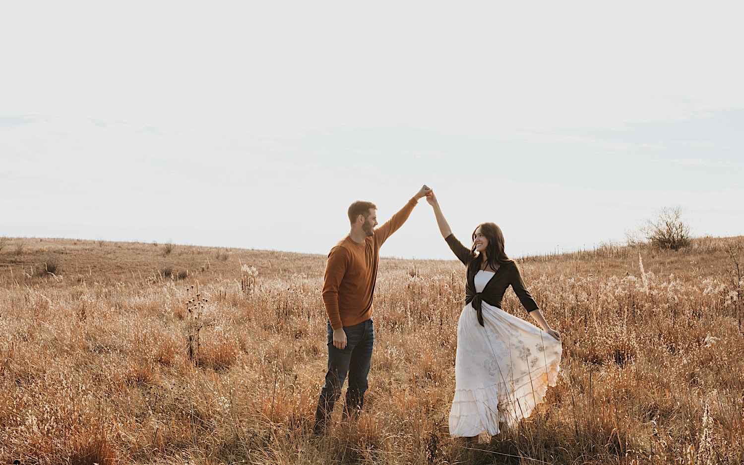A couple in a field dance with one another while holding hands and smiling during their fall engagement session in Minnesota A couple in a field dance with one another while holding hands and smiling during their fall engagement session in Minnesota