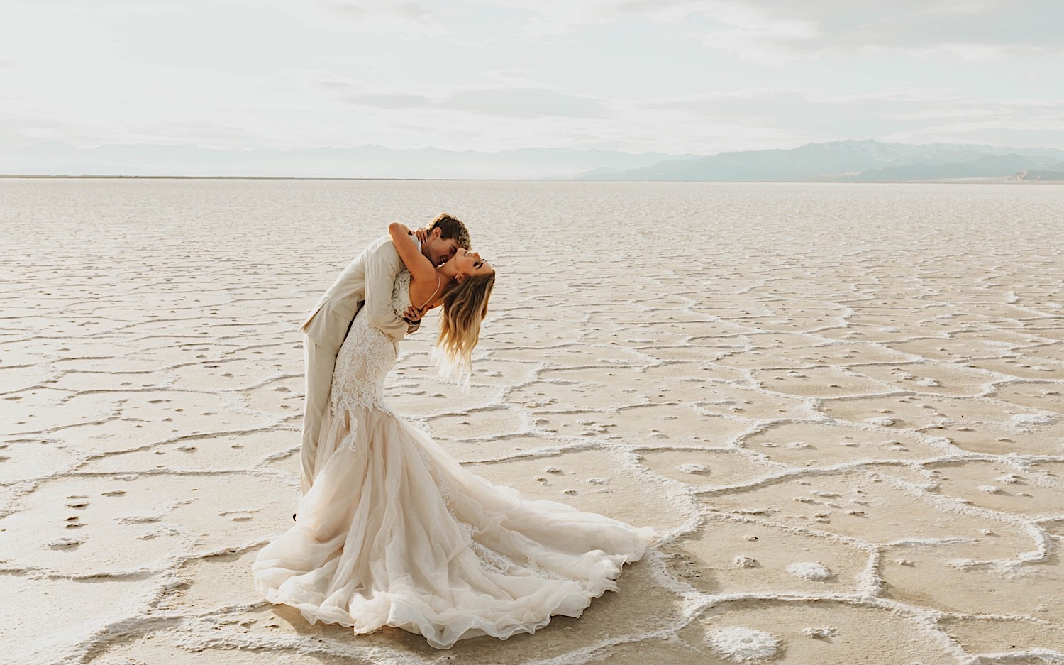 A bride leans back and smiles while the groom kisses her on the neck as the two stand in the Utah Salt Flats on their elopement day
