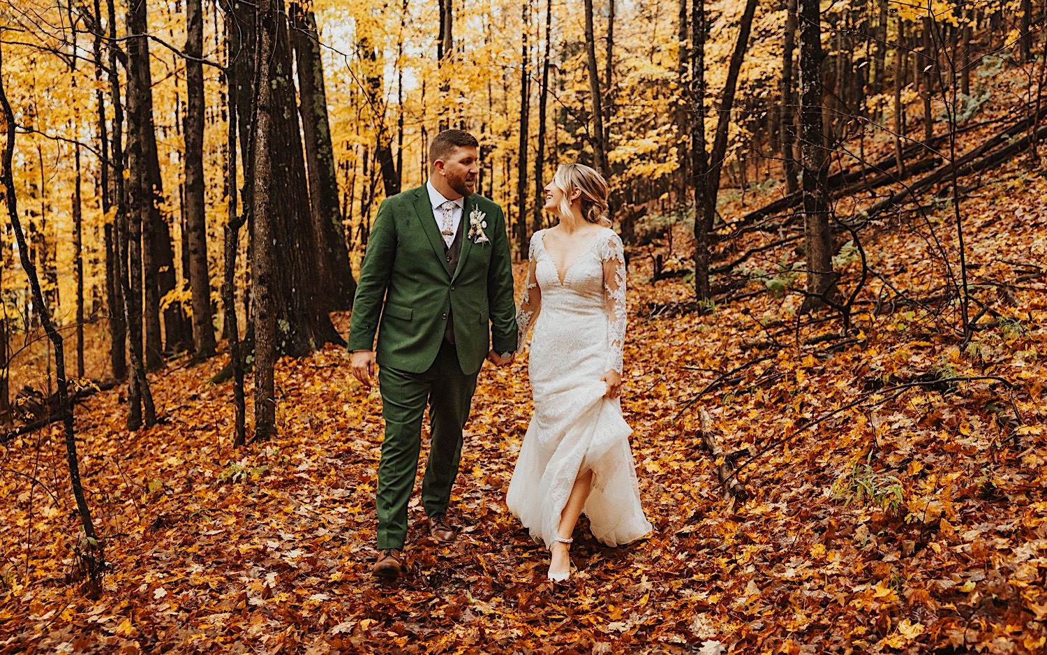 A bride and groom walk through a leaf covered forest in the fall for portraits during their wedding at Lake Bomoseen Lodge in Vermont