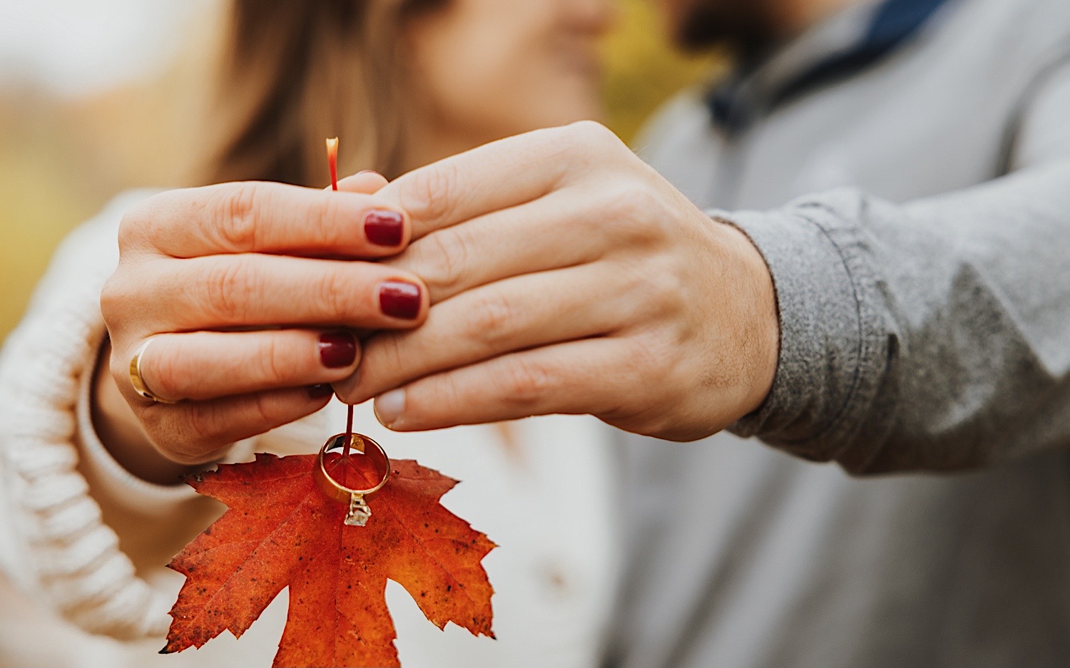 A couple hold out a leaf with their engagement ring resting on the stem during their engagement session at Theodore Wirth Park in Minneapolis