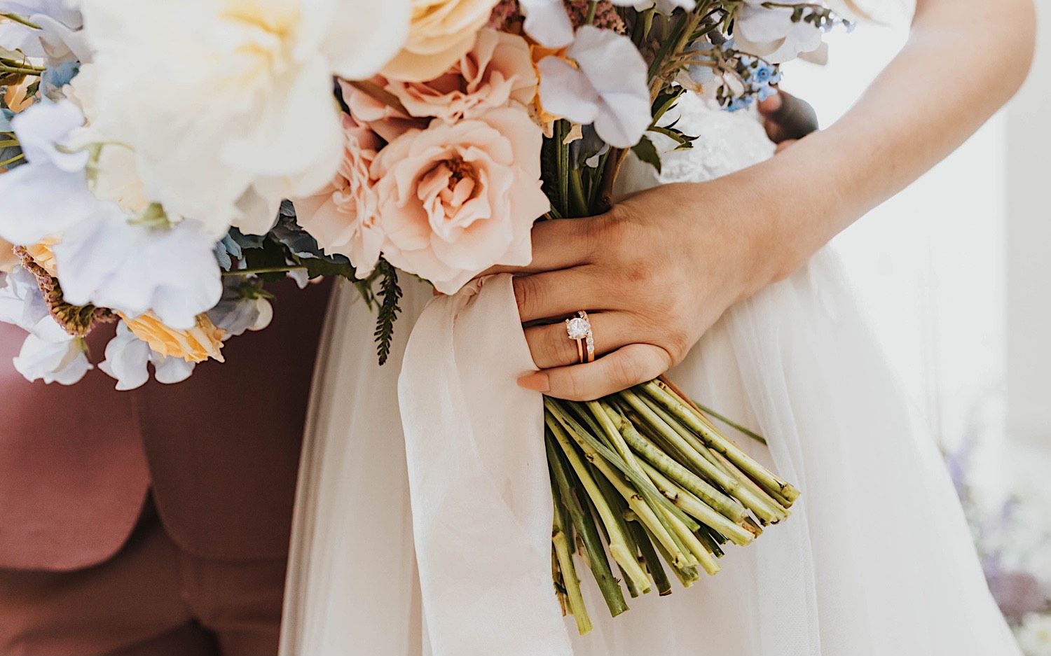 Close up photo of a bride's hand with her wedding ring on it holding her flower bouquet