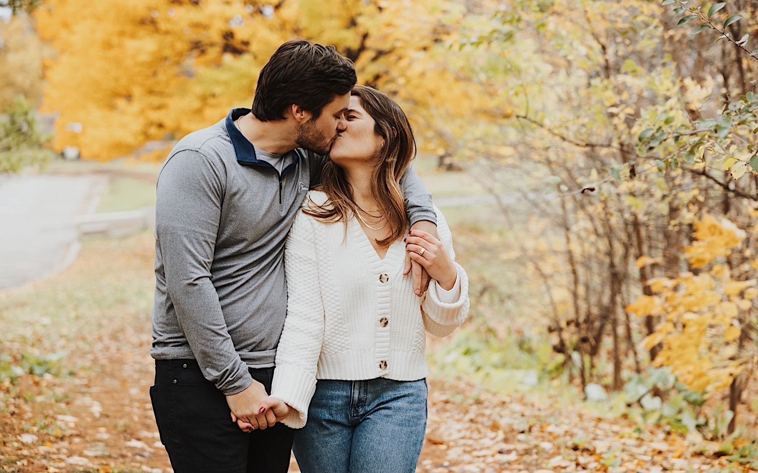 A couple kiss while walking along a path in Theodore Wirth Park in Minneapolis during their engagement session