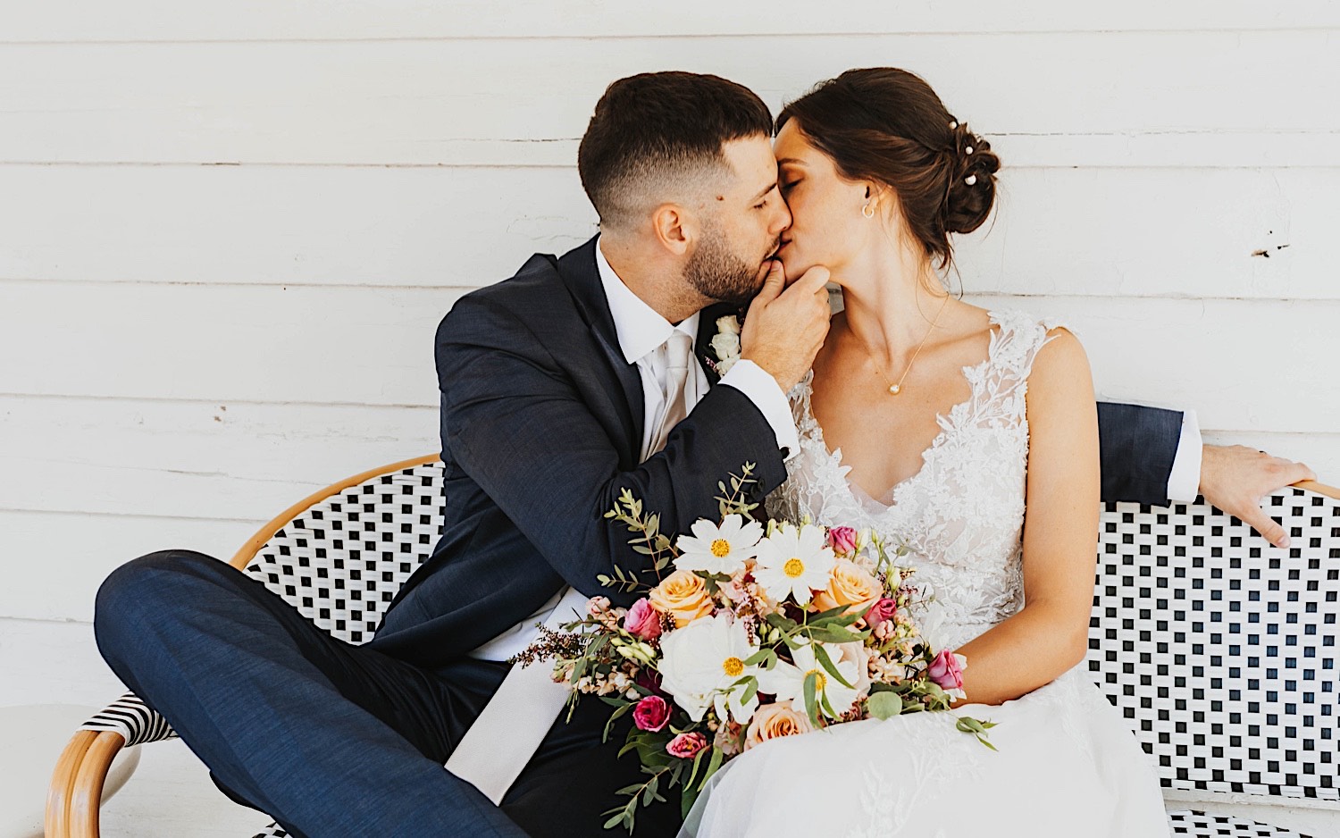 A bride and groom kiss one another while sitting on a bench at their wedding venue Legacy Hill Farm