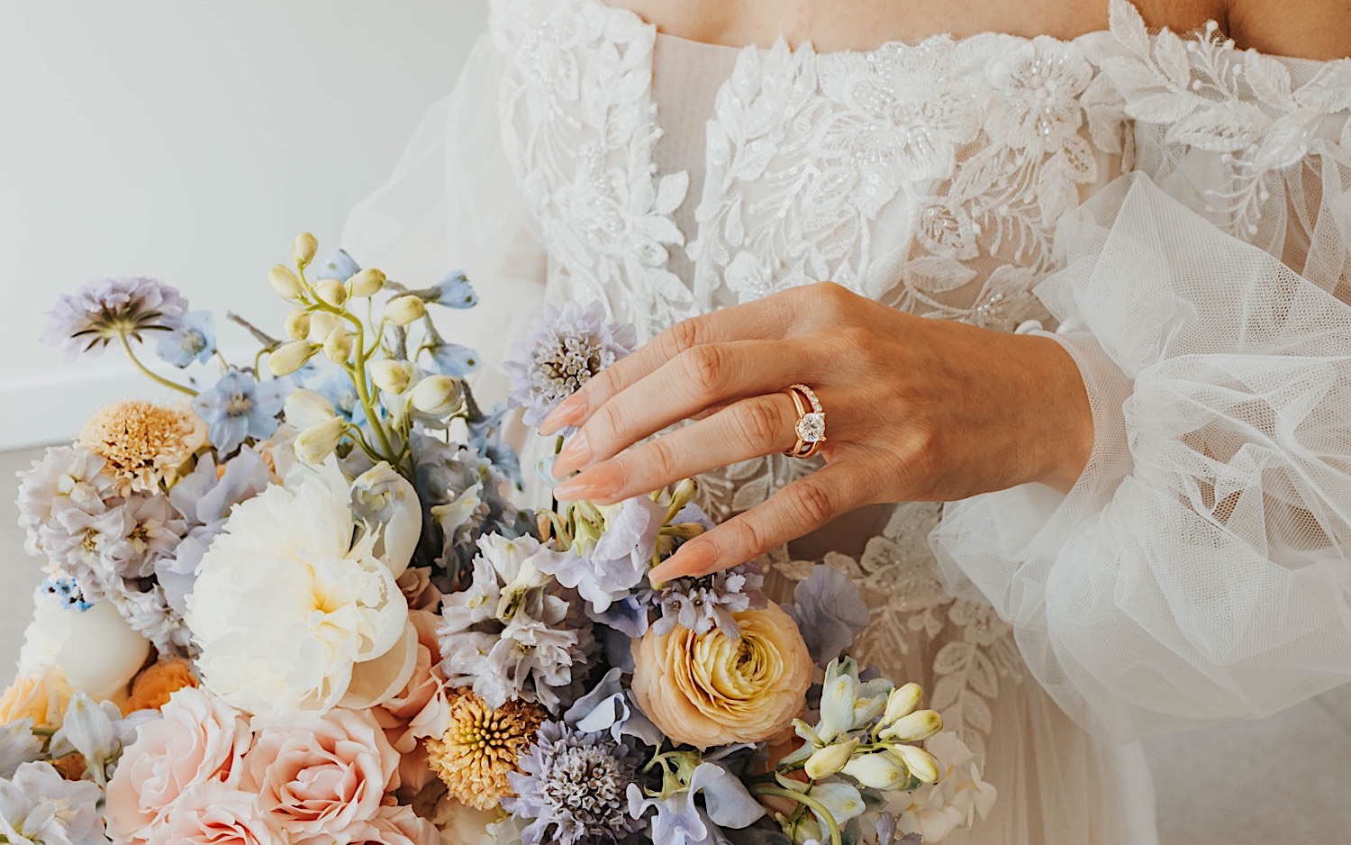 Close up photo of a bride's hand with her wedding ring on it touching her bouquet of flowers