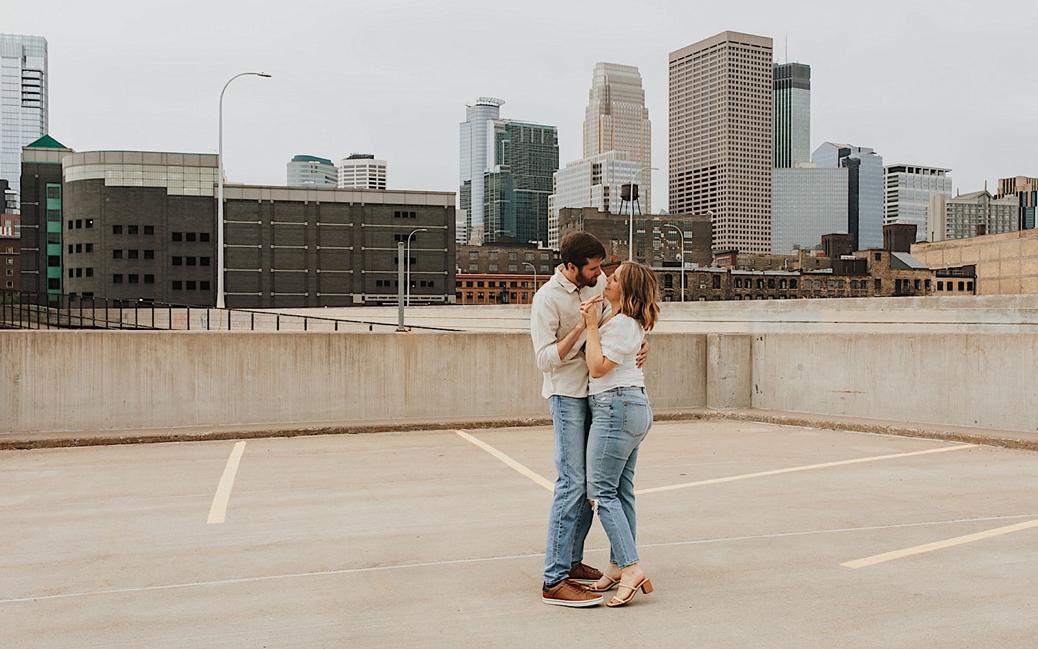 While on the top level of a parking garage in downtown Minneapolis a couple hold hands and dance while having their engagement photos taken