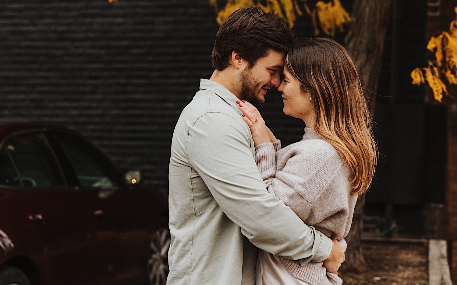 A couple embrace one another in front of a brick wall in Minneapolis' North Loop during their engagement session