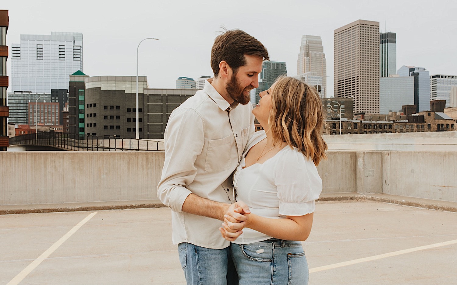 A couple hold hands and smile at one another while having their engagement photos taken on the top level of a parking garage in downtown Minneapolis