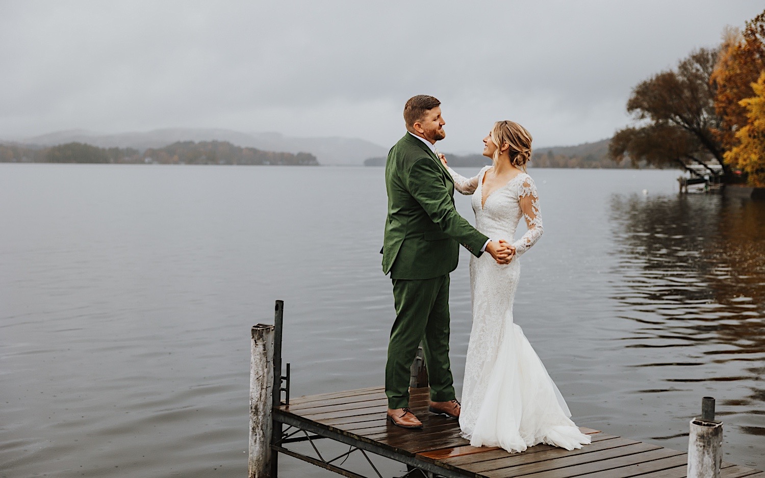 While on a dock on Lake Bomoseen in Vermont, a bride and groom smile at one another while dancing together