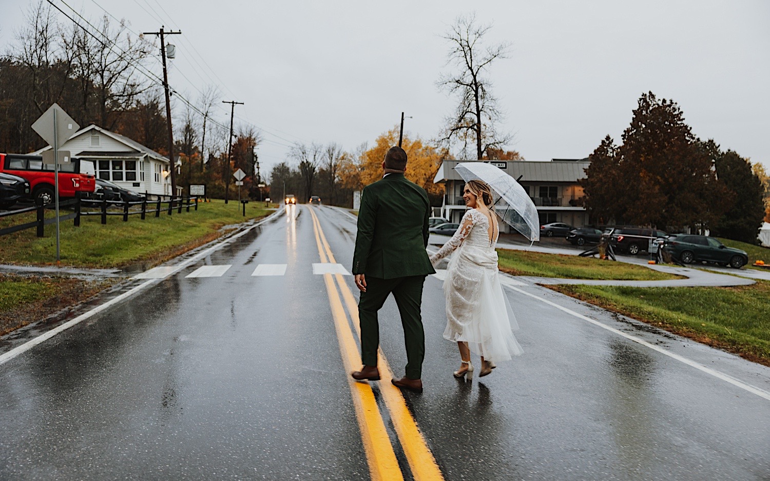 A bride and groom hold hands while crossing a street on a rainy day to get to their wedding venue, Lake Bomoseen Lodge in Vermont