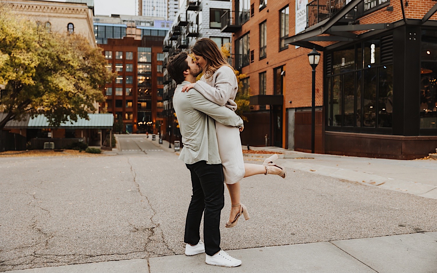 A couple kiss while the woman is lifted in the air by the man during their engagement session in Minneapolis' North Loop