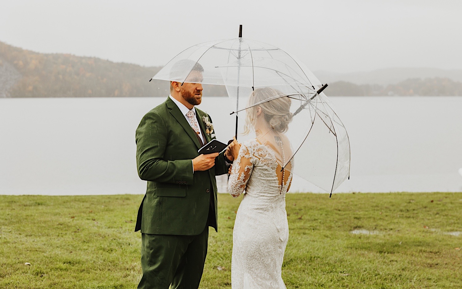 A bride and groom stand under umbrellas and read their private vows to one another while standing next to Lake Bomoseen in Vermont