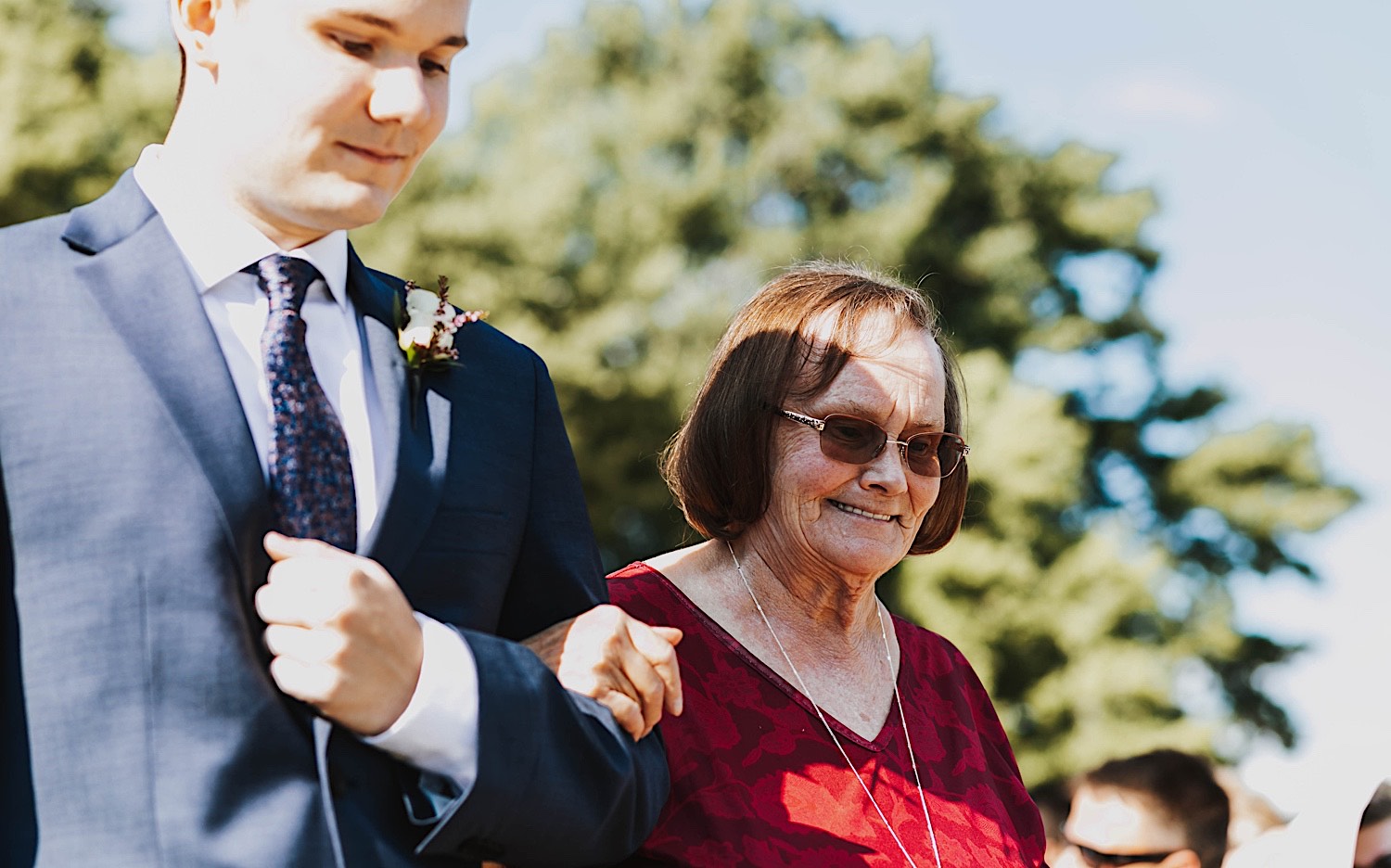 A woman smiles while being walked down the aisle of a wedding ceremony by a man A woman smiles while being walked down the aisle of a wedding ceremony by a man
