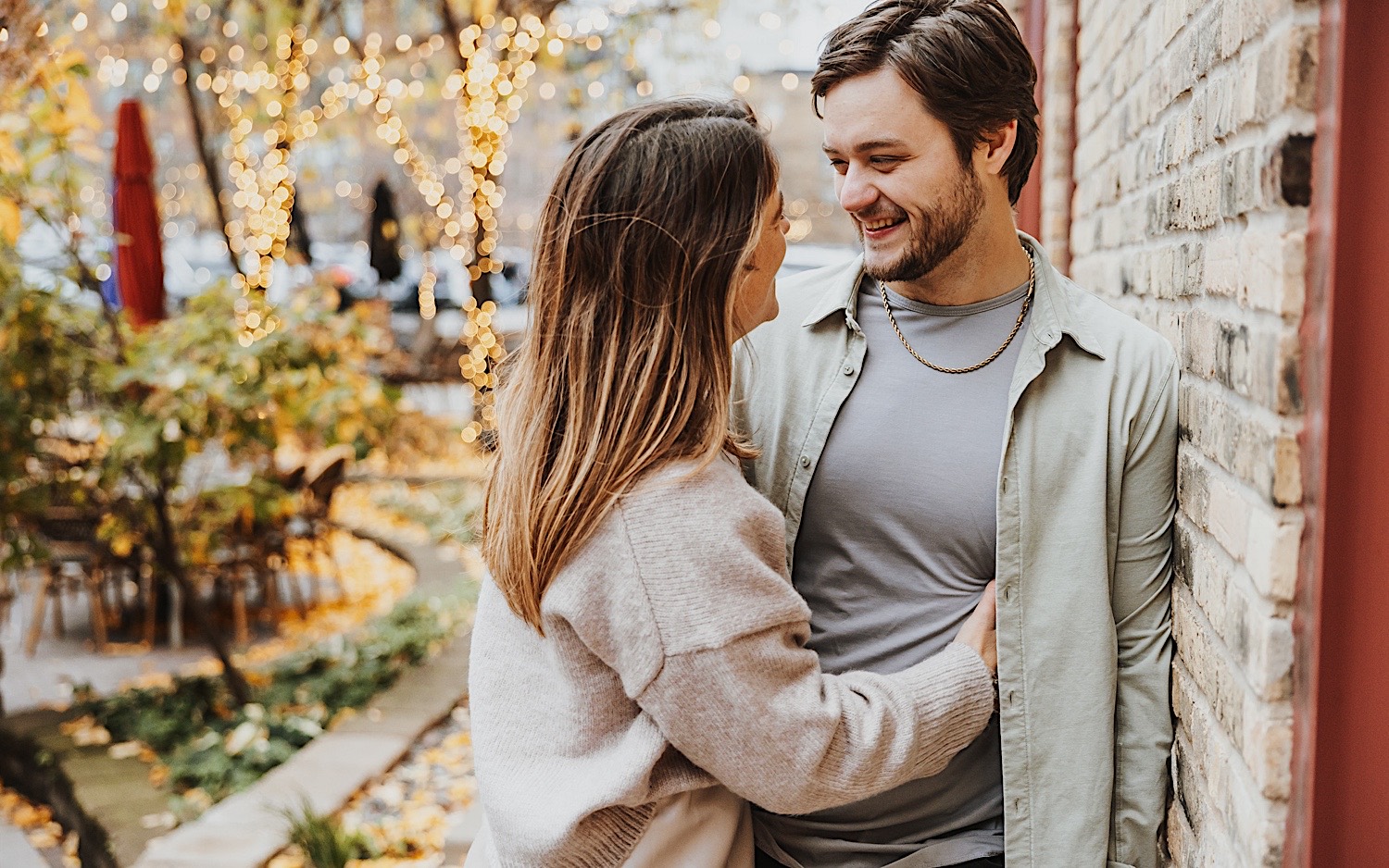 A couple lean against a brick wall and smile at one another while in Minneapolis' North Loop during their engagement session