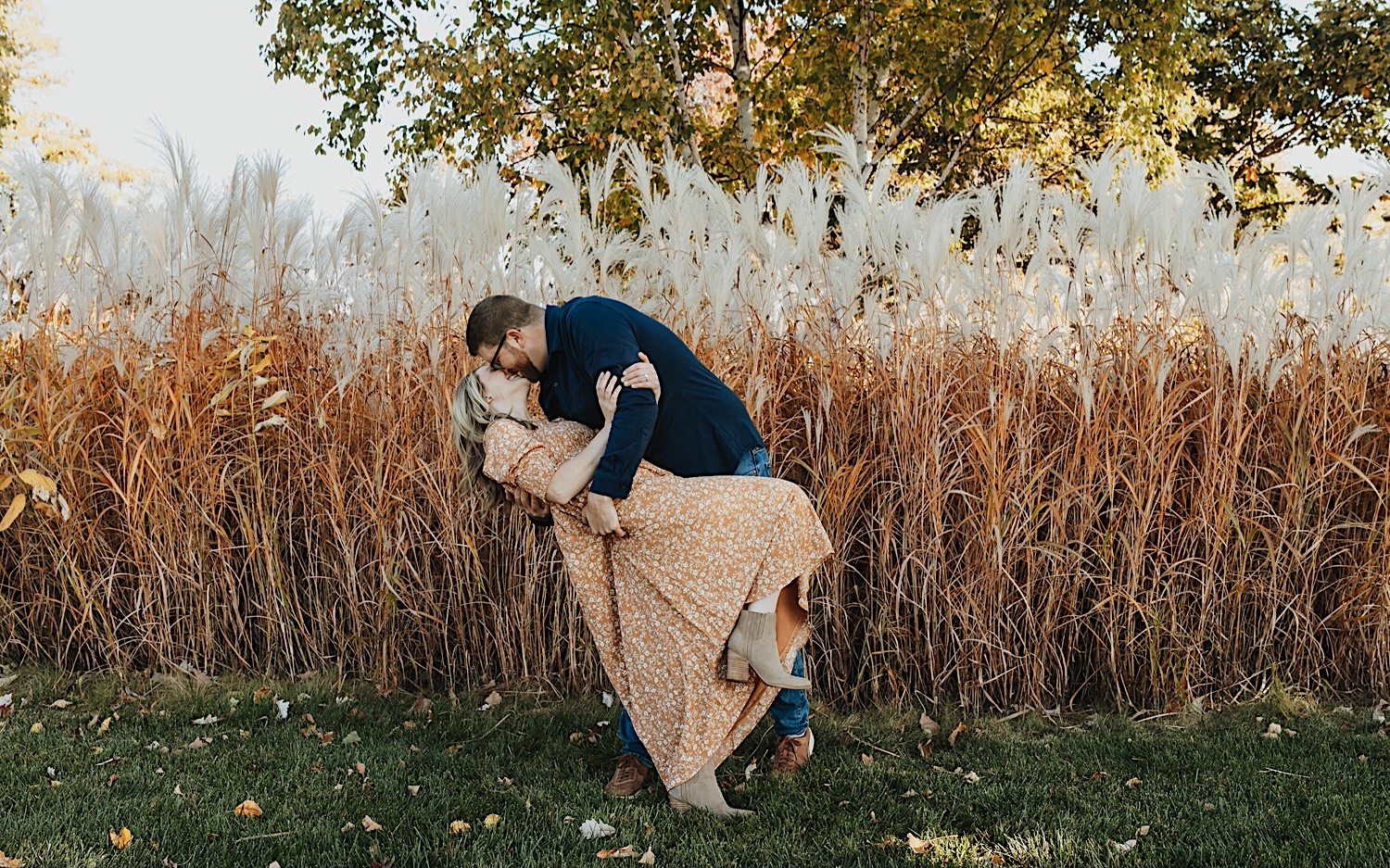 During a fall engagement session in Winona a woman is dipped and kissed by a man as they stand in front of a field