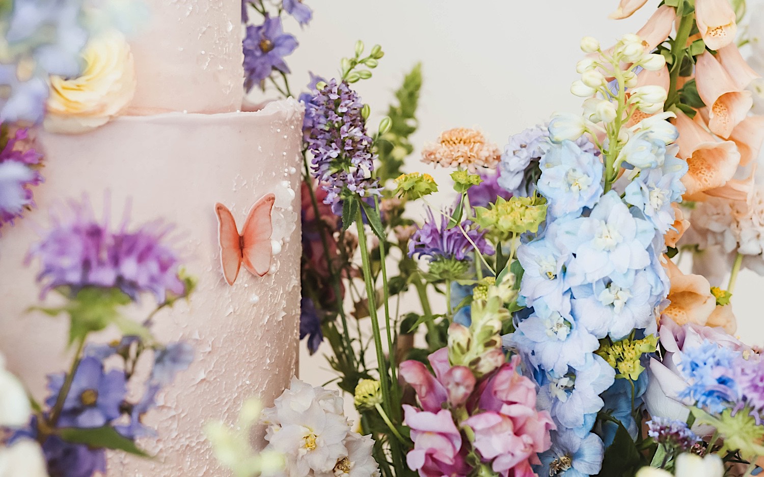 Detail photo of a wedding cake showing off the fake butterflies on it and the flowers surrounding it