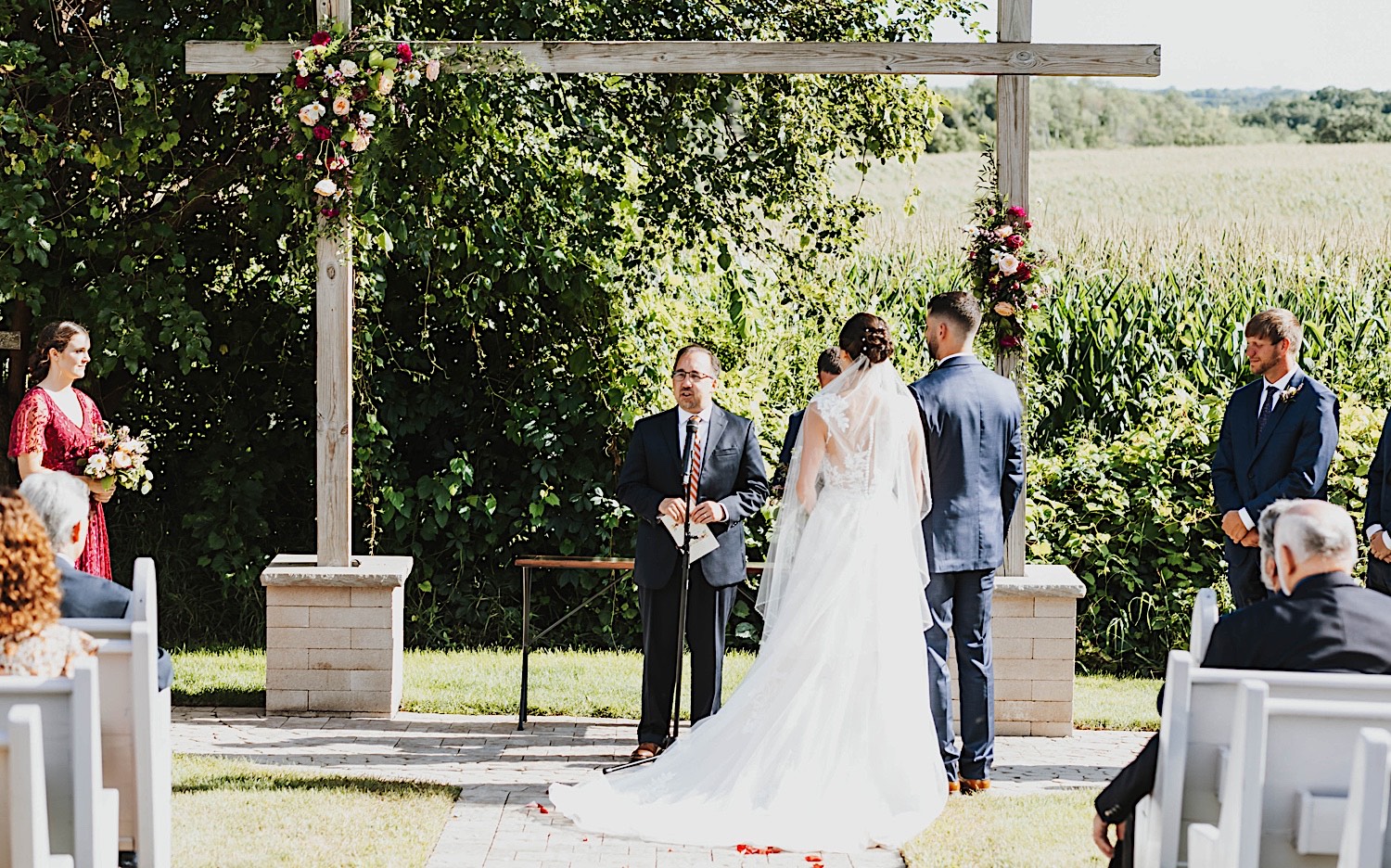 An officiant speaks during an outdoor wedding ceremony while the bride and groom stand side by side at their wedding venue Legacy Hill Farm