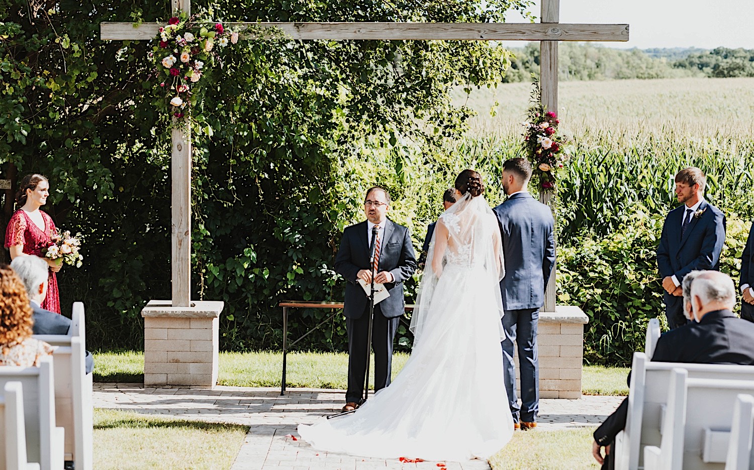 An officiant speaks during an outdoor wedding ceremony while the bride and groom stand side by side at their wedding venue Legacy Hill Farm An officiant speaks during an outdoor wedding ceremony while the bride and groom stand side by side at their wedding venue Legacy Hill Farm