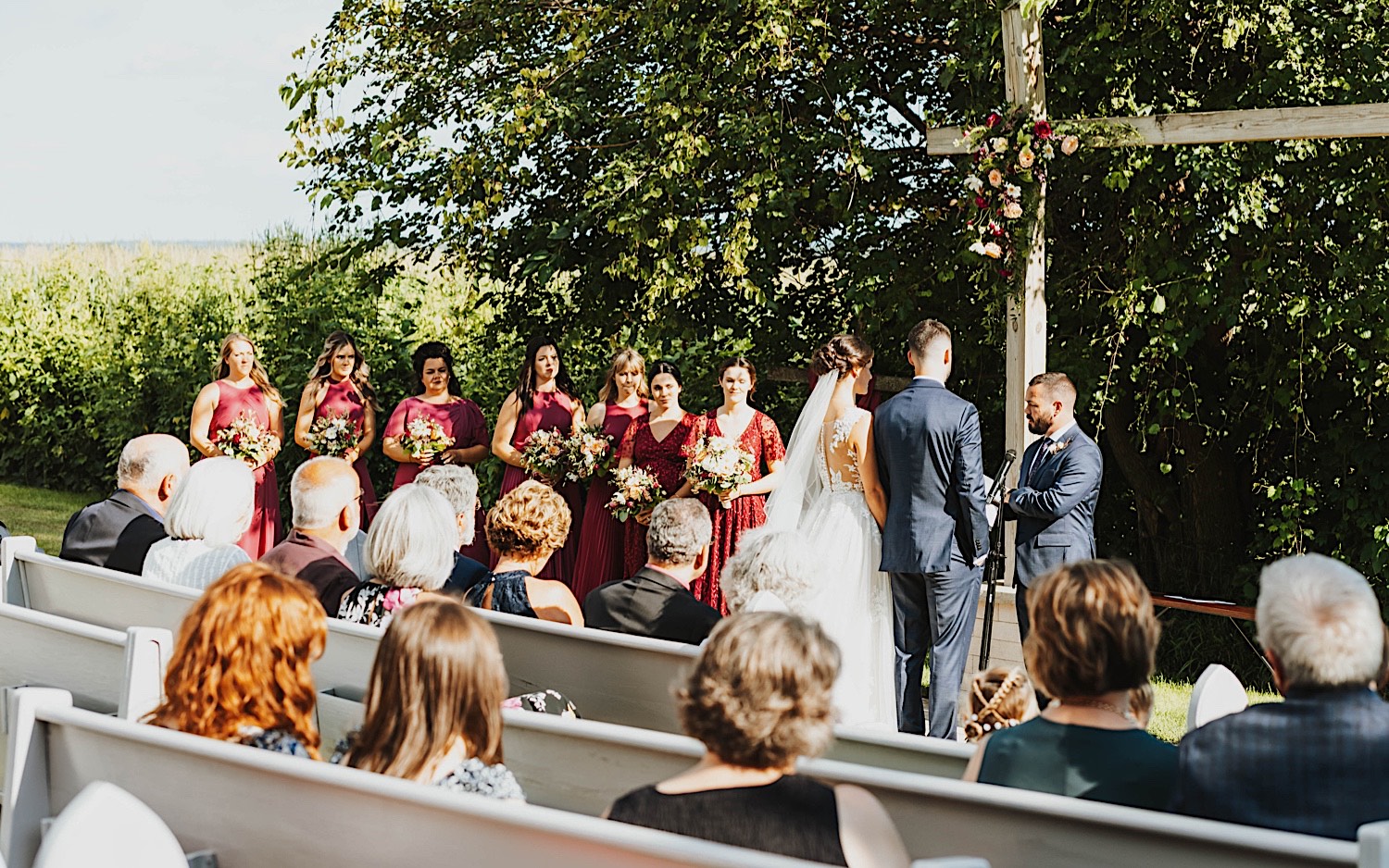 A bride and groom stand side by side during their outdoor wedding ceremony at Legacy Hill Farm while guests watch