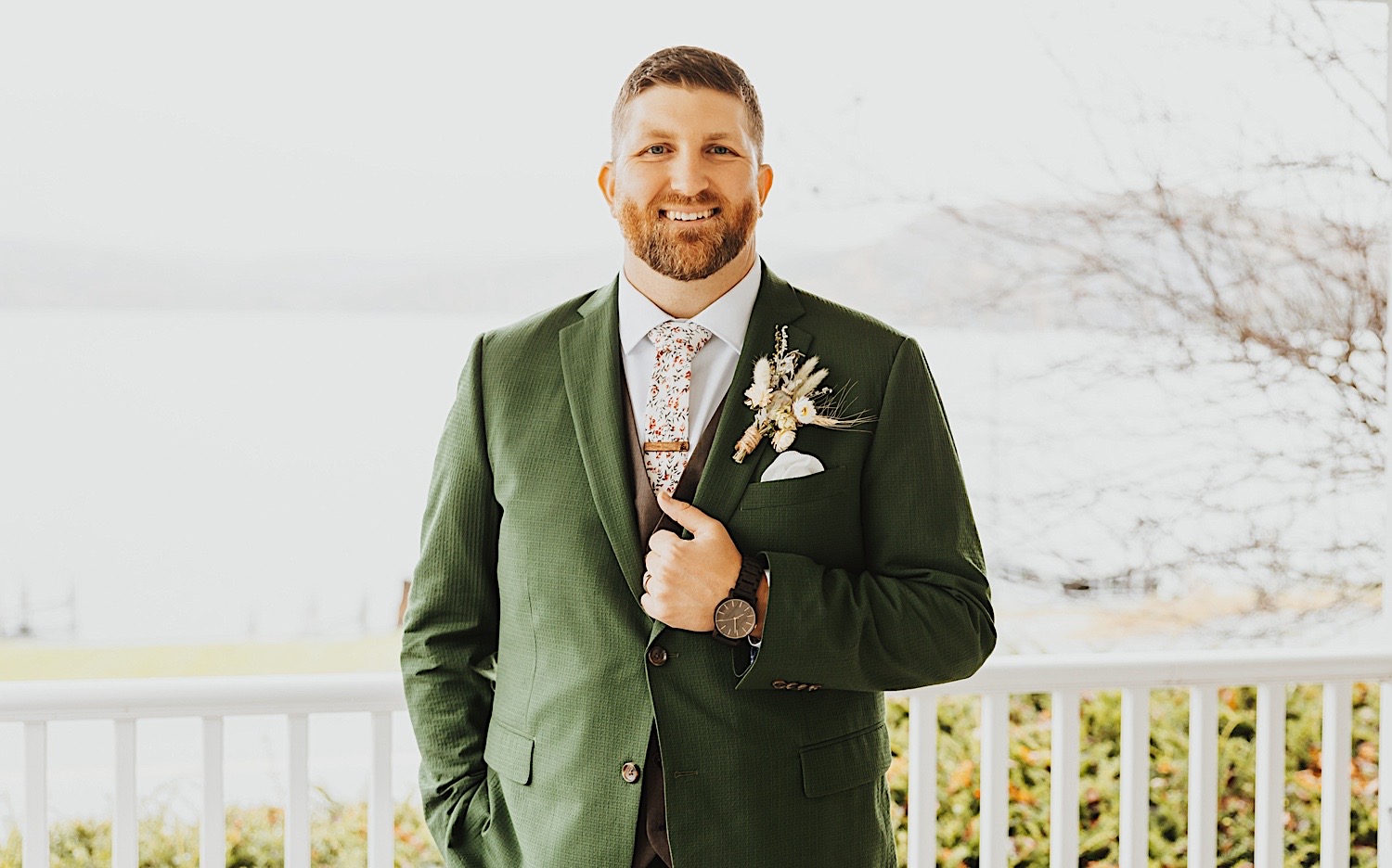 Portrait photo of a groom smiling at the camera and holding his suit coat while standing on a front patio of a home on Lake Bomoseen in Vermont