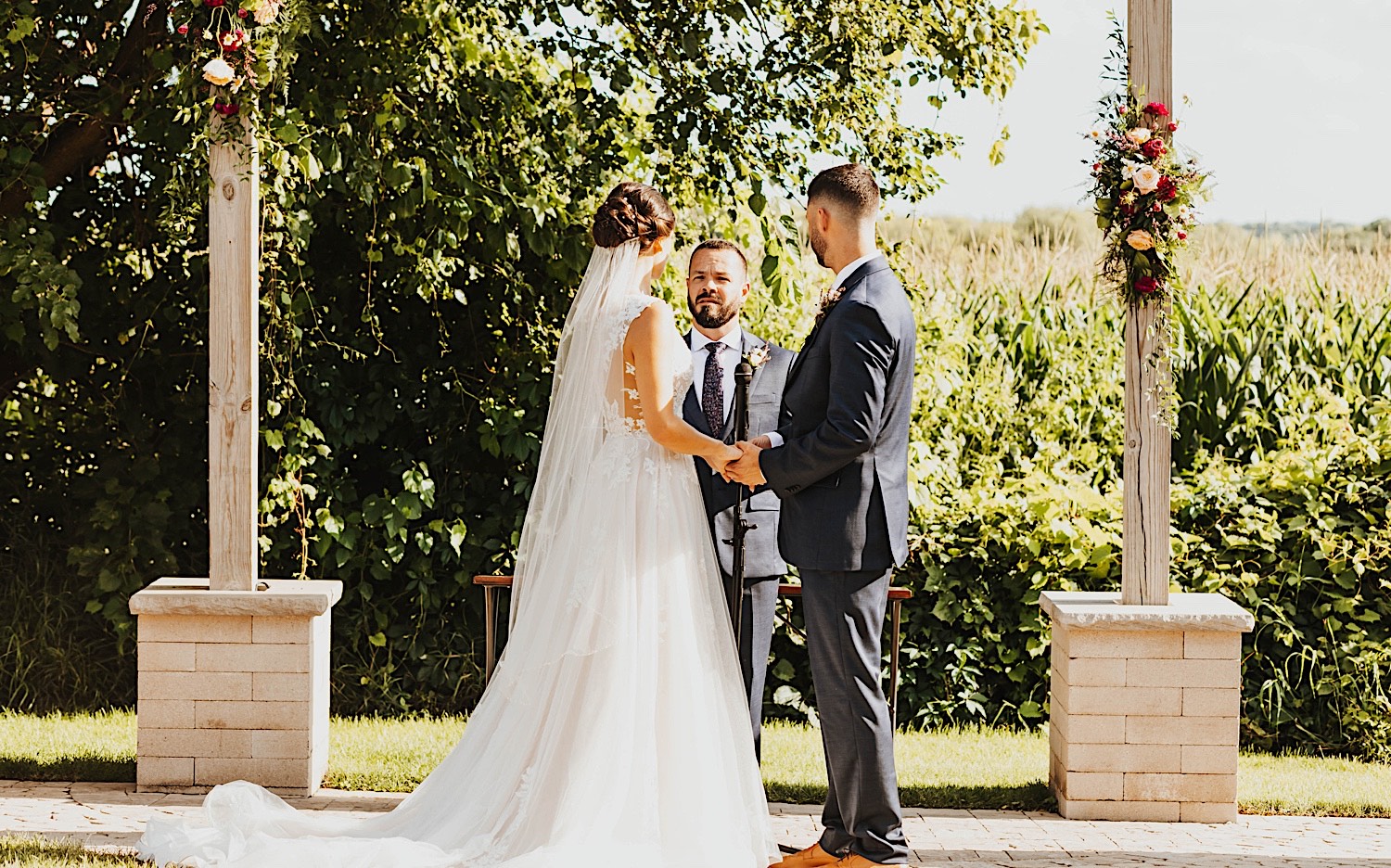 A bride and groom hold hands while their officiant speaks during their outdoor wedding ceremony at Legacy Hill Farm