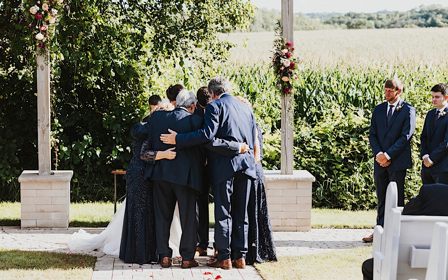 A family huddles around one another for a prayer during an outdoor wedding ceremony at Legacy Hill Farm