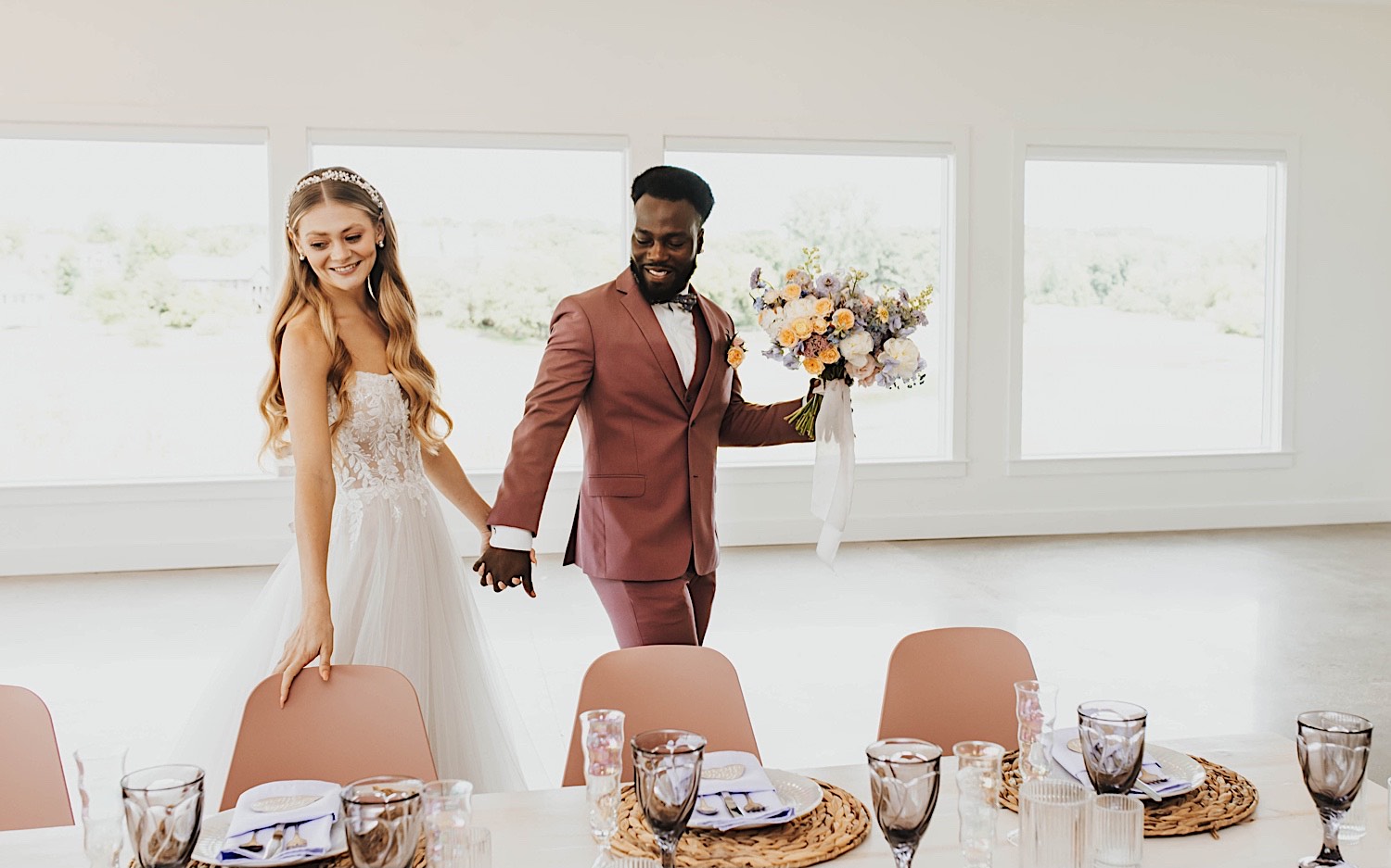 A bride and groom walk hand in hand while looking at a table decorated for their wedding reception at The Aisling