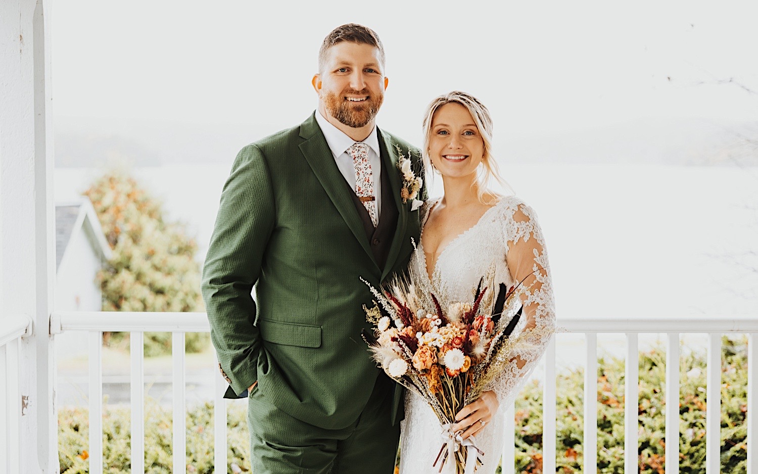 Portrait  photo of a bride and groom smiling at the camera while standing next to one another on a front porch of a home at Lake Bomoseen in Vermont