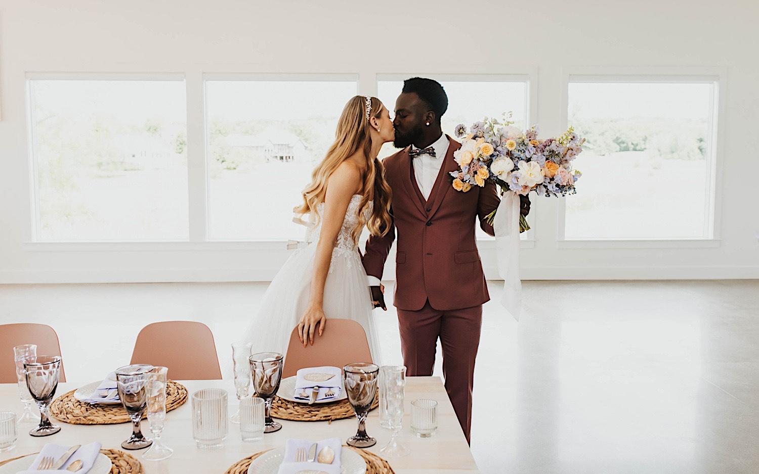 A bride and groom kiss one another while standing next to their table for their wedding reception at The Aisling