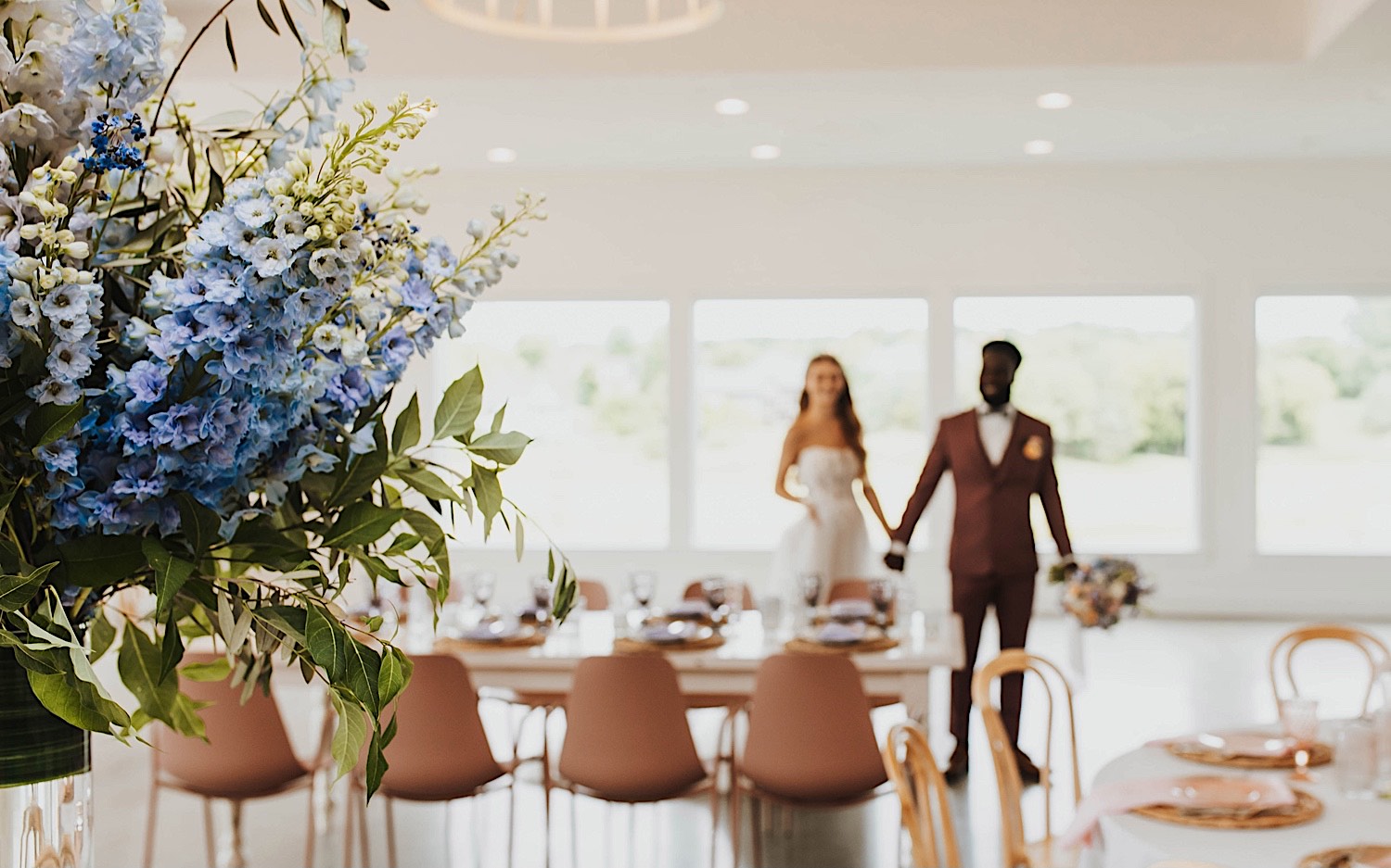 Close up photo of flowers in the wedding reception space at The Aisling, in the background out of focus are the bride and groom holding hands