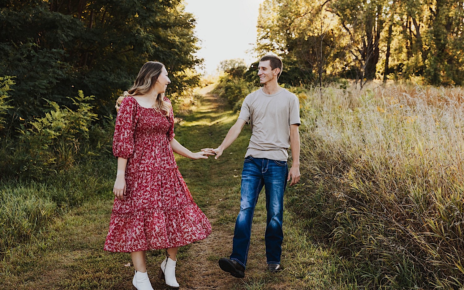 A couple on a grass path between a field and a forest smile at one another and hold hands A couple on a grass path between a field and a forest smile at one another and hold hands