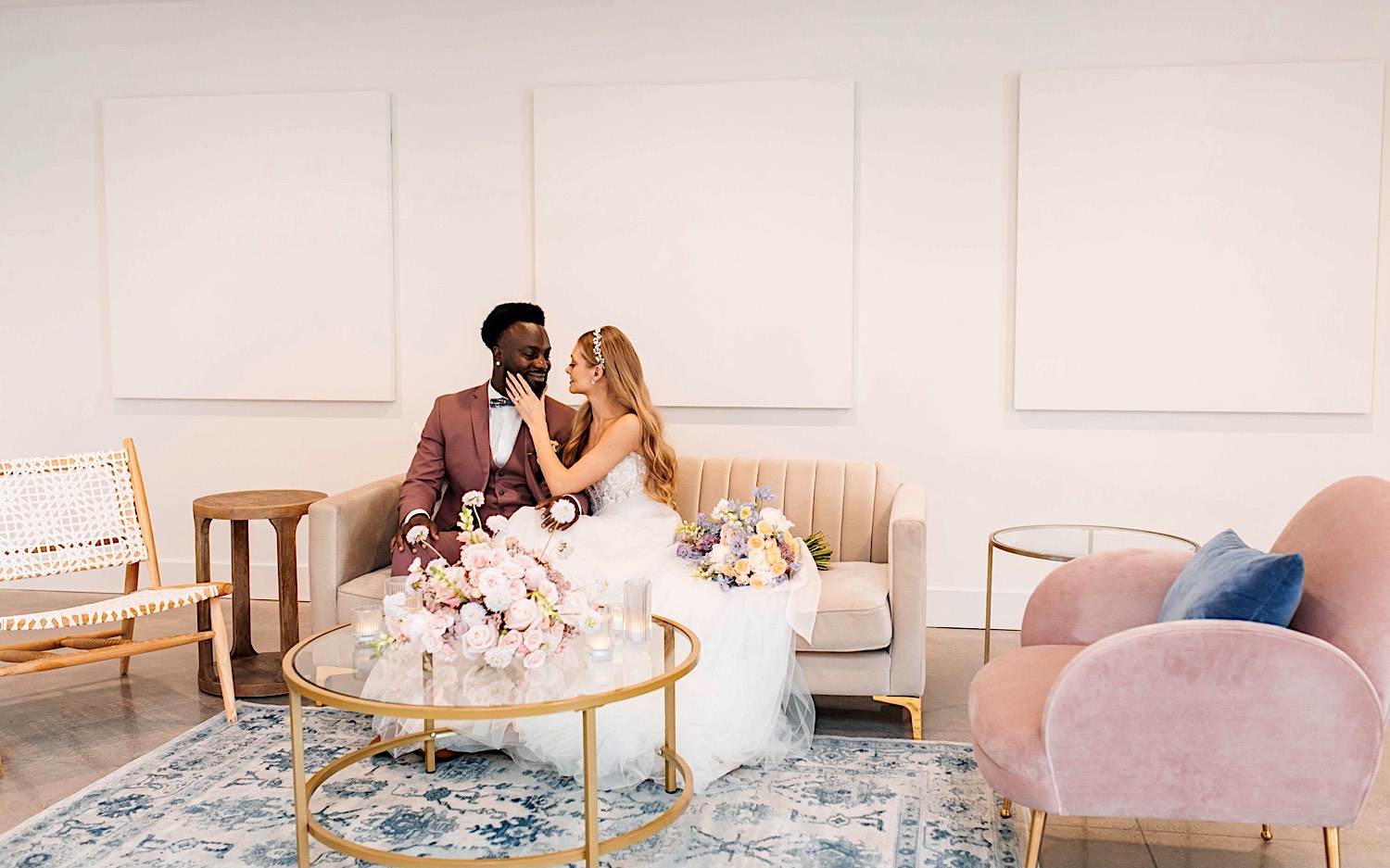 A bride and groom sit next to one another on a couch as the bride touches the groom's face during their wedding day at The Aisling