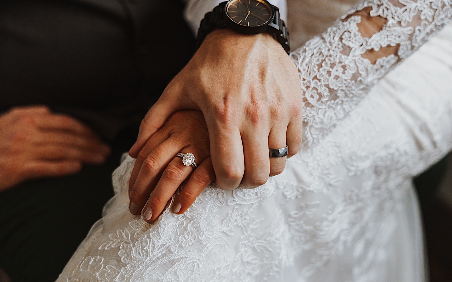 Close up photo of a bride and groom's hand's holding one another while on the bride's lap showing off their wedding rings