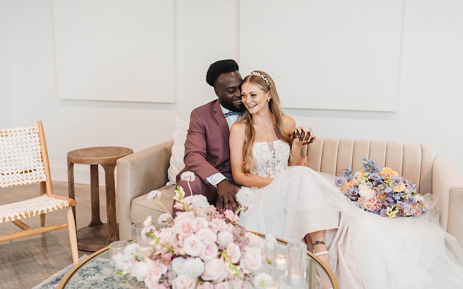 A bride and groom laugh while sitting next to one another on a couch during their wedding day at The Aisling