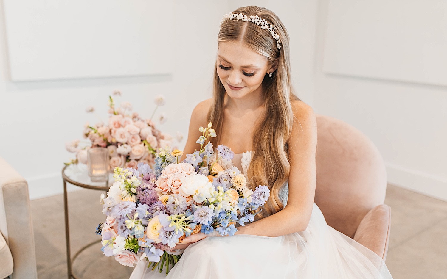 A bride sits in a chair and looks down at her flower bouquet during her wedding day at The Aisling