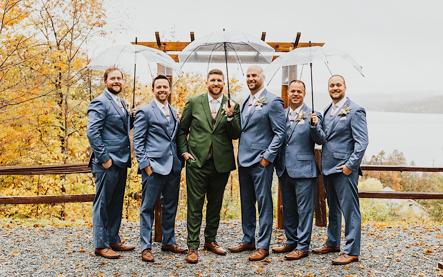 A groom stands with his 5 groomsmen for a portrait photo in the rain at the outdoor ceremony space of Lake Bomoseen Lodge in Vermont