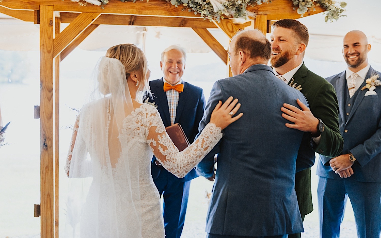 A bride and groom both put their hands on the back of the bride's father after he escorted her down the aisle for her wedding ceremony at Lake Bomoseen Lodge in Vermont