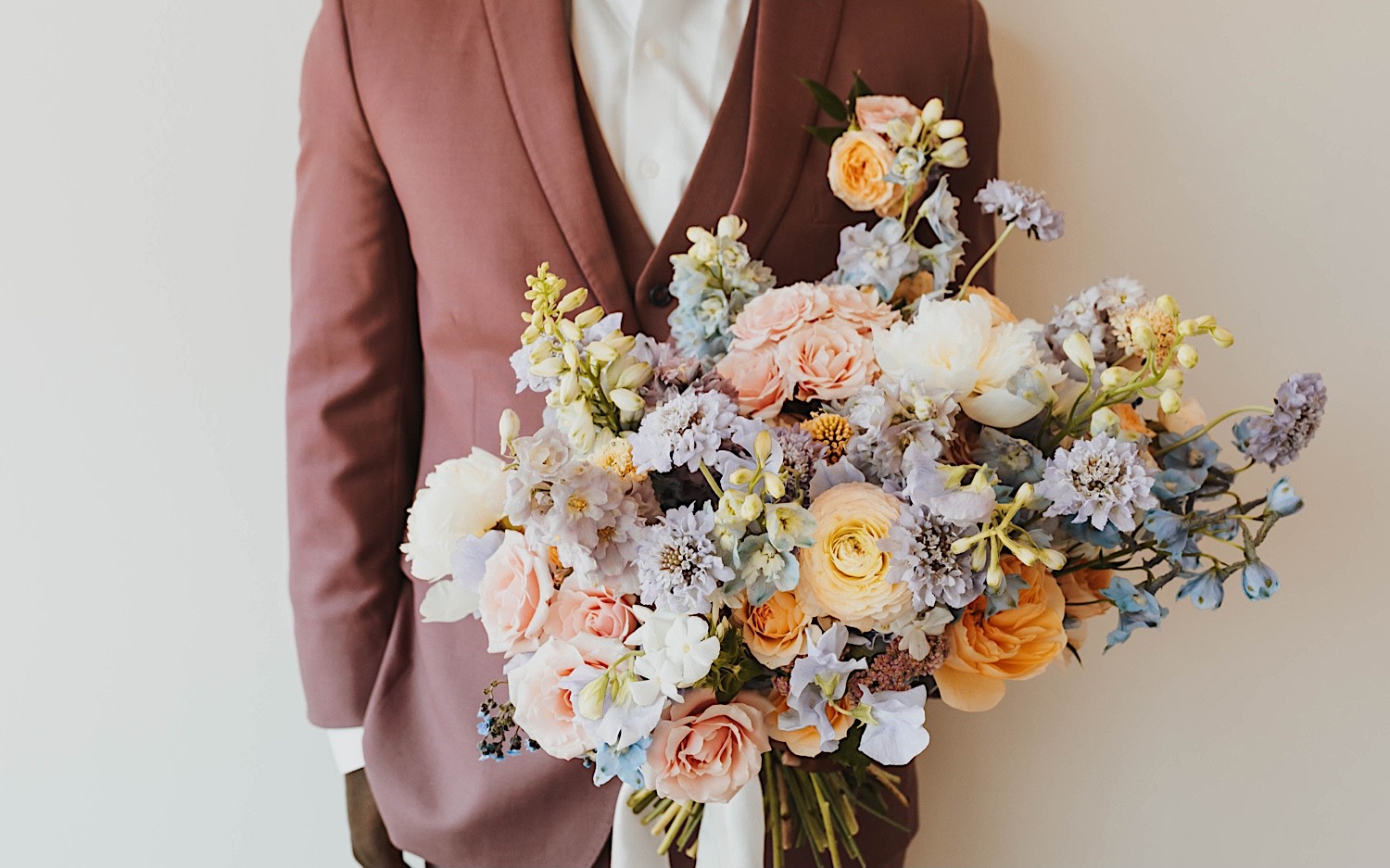 Torso photo of a groom standing and holding a flower bouquet towards the camera Torso photo of a groom standing and holding a flower bouquet towards the camera