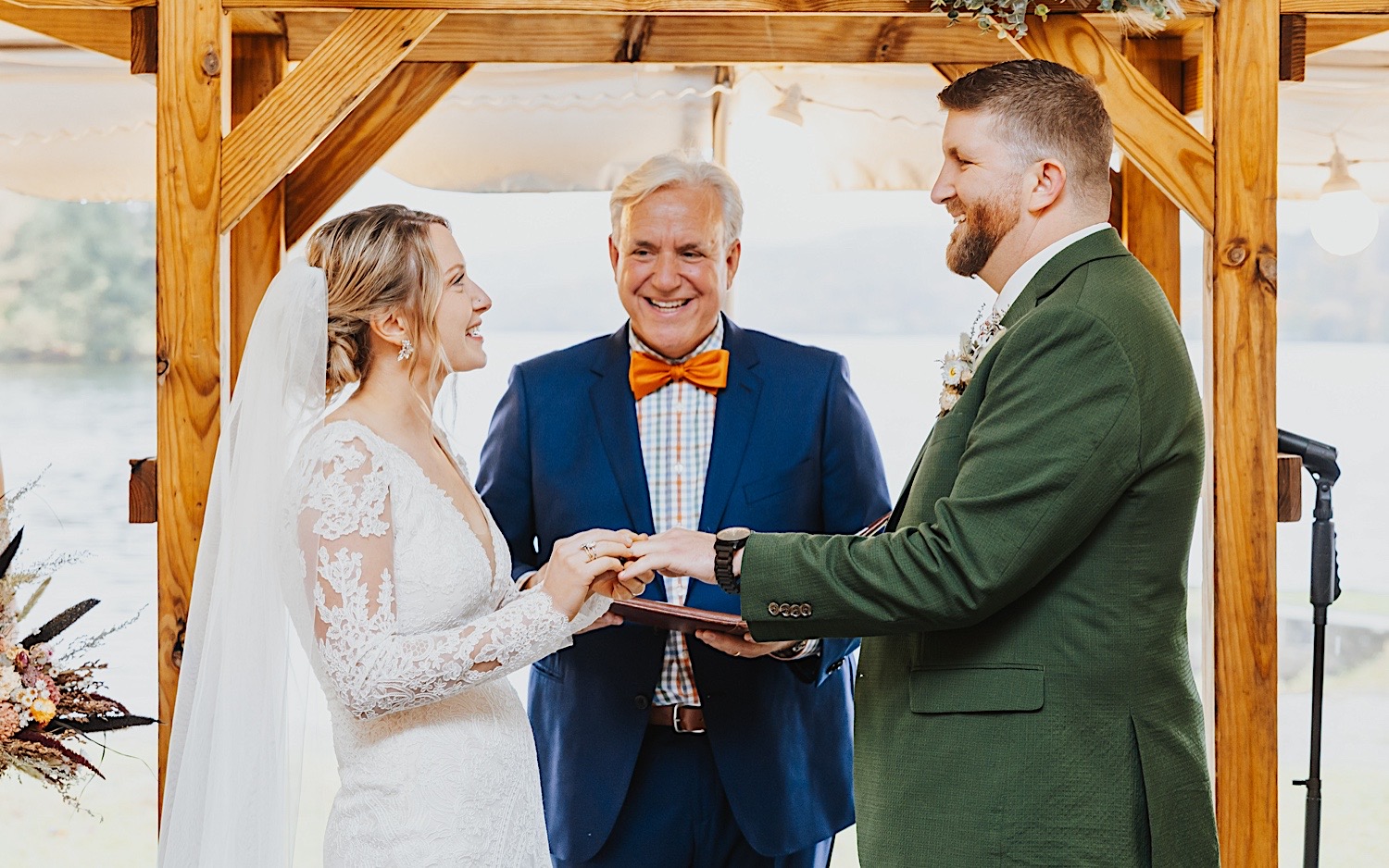 A bride and groom smile at each other while the bride puts a wedding ring on the groom's hand during their rainy wedding ceremony at Lake Bomoseen Lodge in Vermont