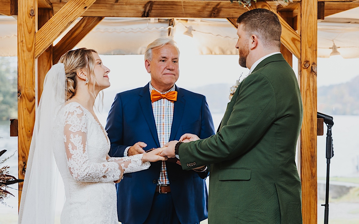 A bride and groom look at one another while holding hands as their officiant speaks during their wedding ceremony under a tent during a rainy day at Lake Bomoseen Lodge in Vermont