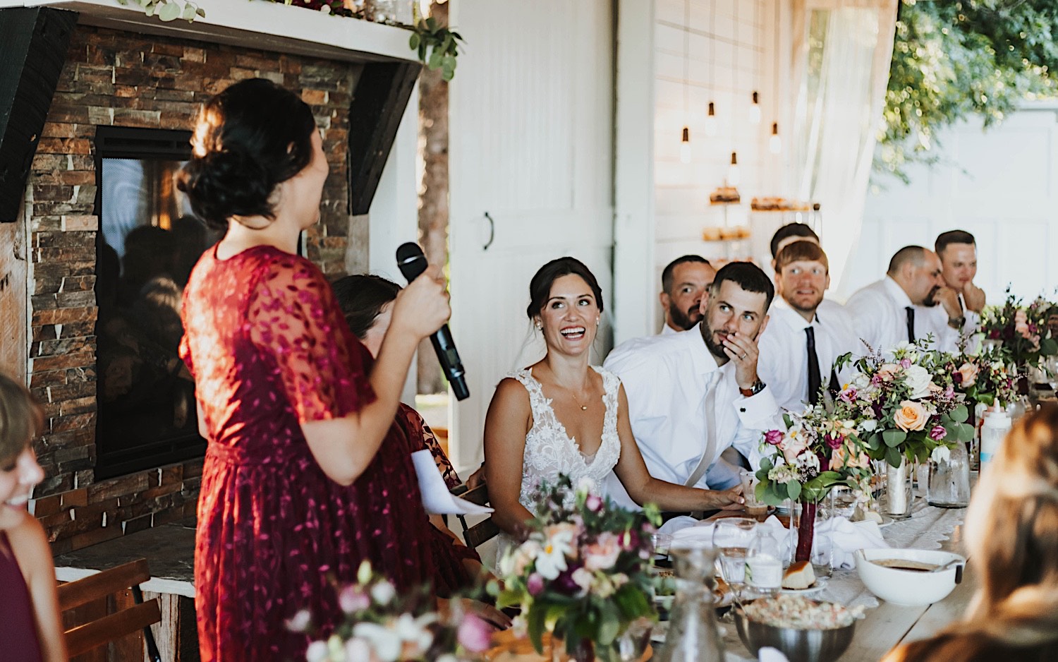 A bride smiles while sitting and listening to a bridesmaid give a speech during her wedding reception at Legacy Hill Farm A bride smiles while sitting and listening to a bridesmaid give a speech during her wedding reception at Legacy Hill Farm