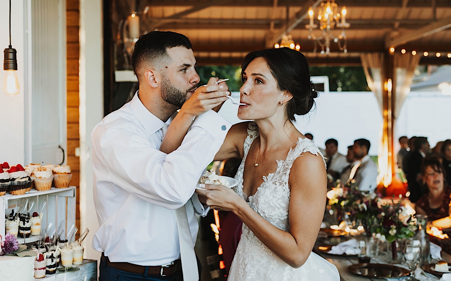 A bride and groom intertwine arms as they feed one another a piece of cake during their wedding reception at Legacy Hill Farm